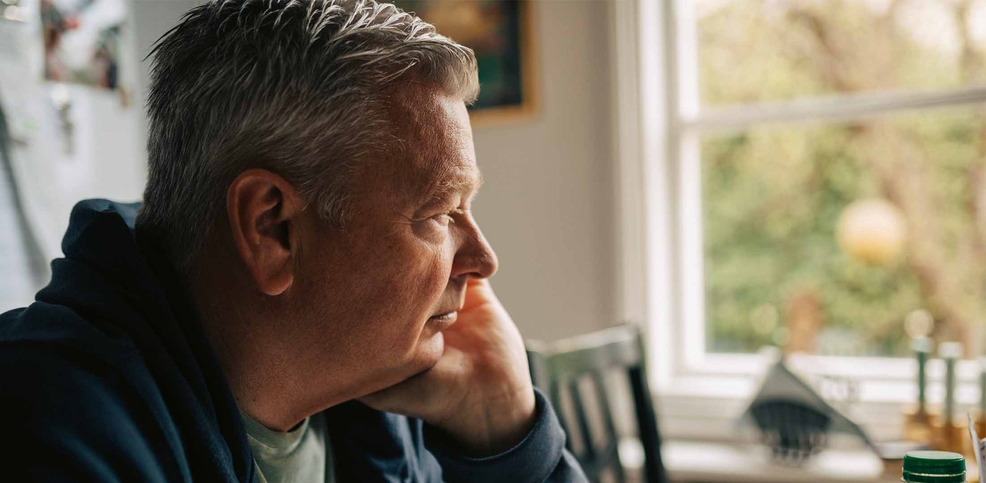 Mandlig pårørende til kræftsyg partner sidder tankefuldt ved køkkenbordet.
