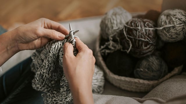 Nærbillede af kvindehænder, der bruger strikning som afledning, når man kæmper med fatigue.
