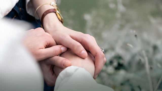 Nærbillede af to personers hænder, der omsorgsfuldt holder hinanden i hånden. 