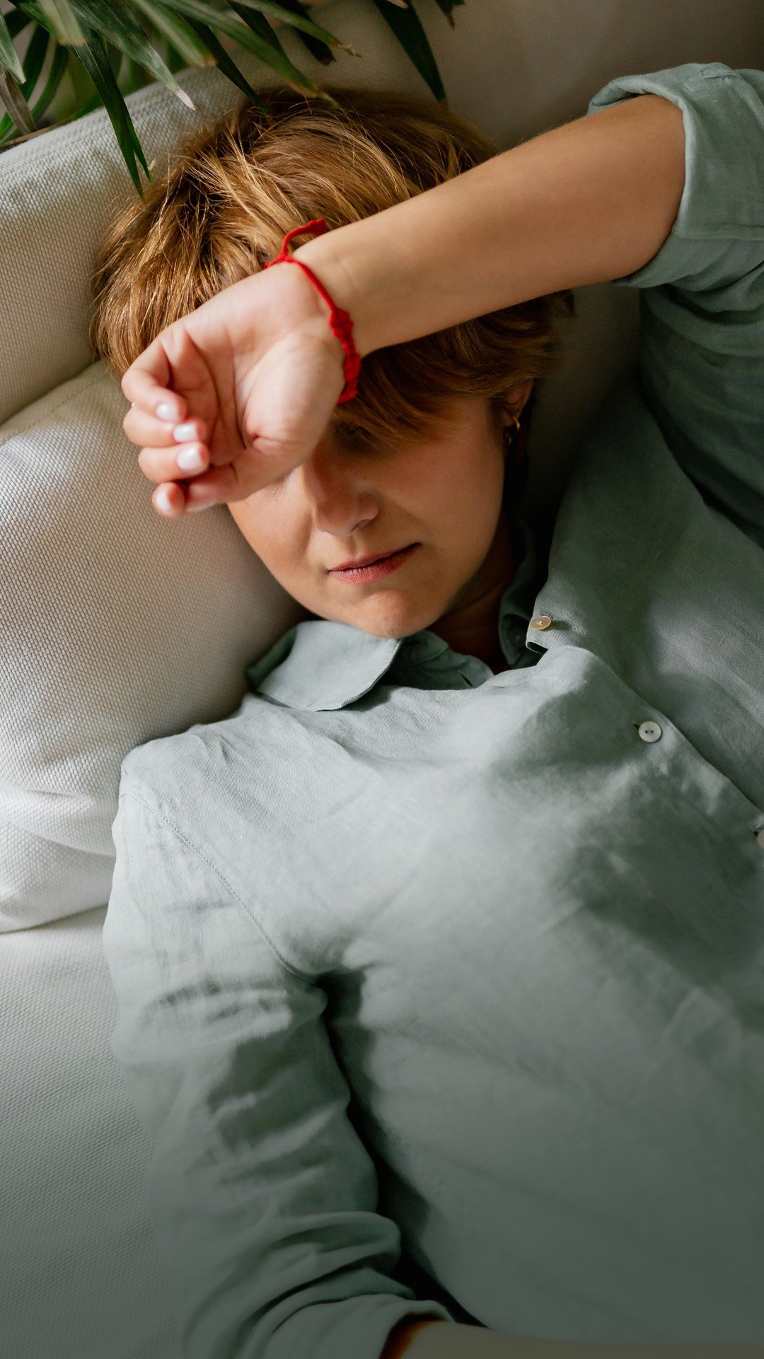 Brystkræftsyg kvinde ligger på sofaen med armen foran øjnene og er tydeligt udmattet. Foto.