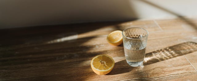 Et glas vand og to halve citroner på et træbord – enkle hjælpemidler mod kvalme ved kræftbehandling.