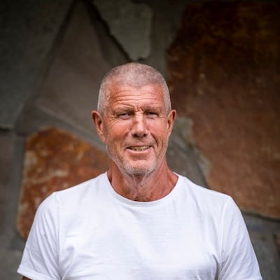 Portrætfoto af enkemanden Stein Tore Haavimb set fra livet og op. Han står foran en murstensvæg og har en hvid T-shirt på.