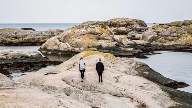 To personer går tur på klipperne ved havet. Illustrationsfoto
