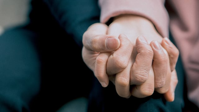 Nærbillede af to, der holder hænder. Fingrene er flettede sammen. Illustrationsfoto