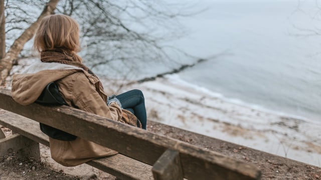 Kvinde der er ramt af træthed fra kræftsygdom, sidder på en bænk og ser ud over vandet. Illustrationsfoto