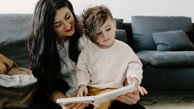 En mor med anden etnisk baggrund og brystkræft med spredning læser en bog for sønnen, der sidder på skødet. Illustrationsfoto