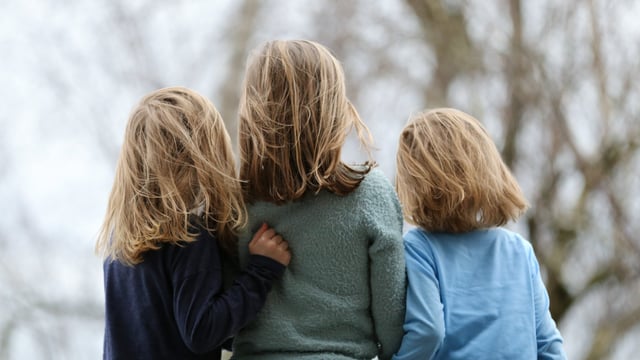 Tre børn, der er pårørende til stadie 4 brystkræft, står tæt sammen ude i nauren på efteråret, med ryggen mod kameraet. Illustrationsfoto