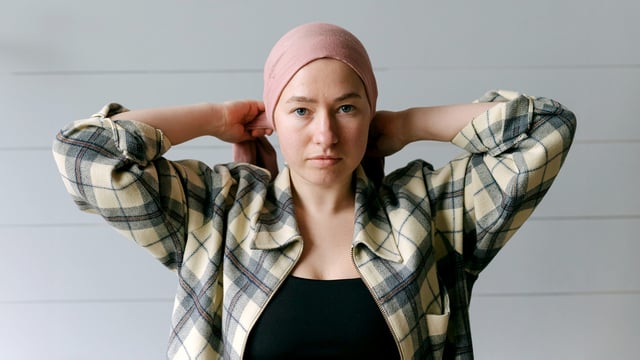 Kvinde binder et sjal omkring sit hoved. Hun har ikke hår på grund af brystkræft. Kvinden ser direkte ind i kameraet. Illustrationsfoto