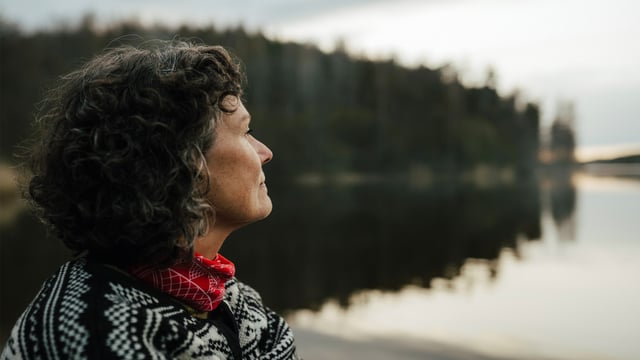 Kvinde med brystkræft med spredning ser ud over en stille sø. Illustrationsfoto