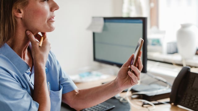 Kvindelig kræftlæge sidder på kontoret og ser på sin mobiltelefon. Illustrationsfoto