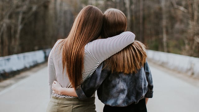 To veninder står side om side og holder om hinanden. Vi ser deres rygge. Illustrationsfoto